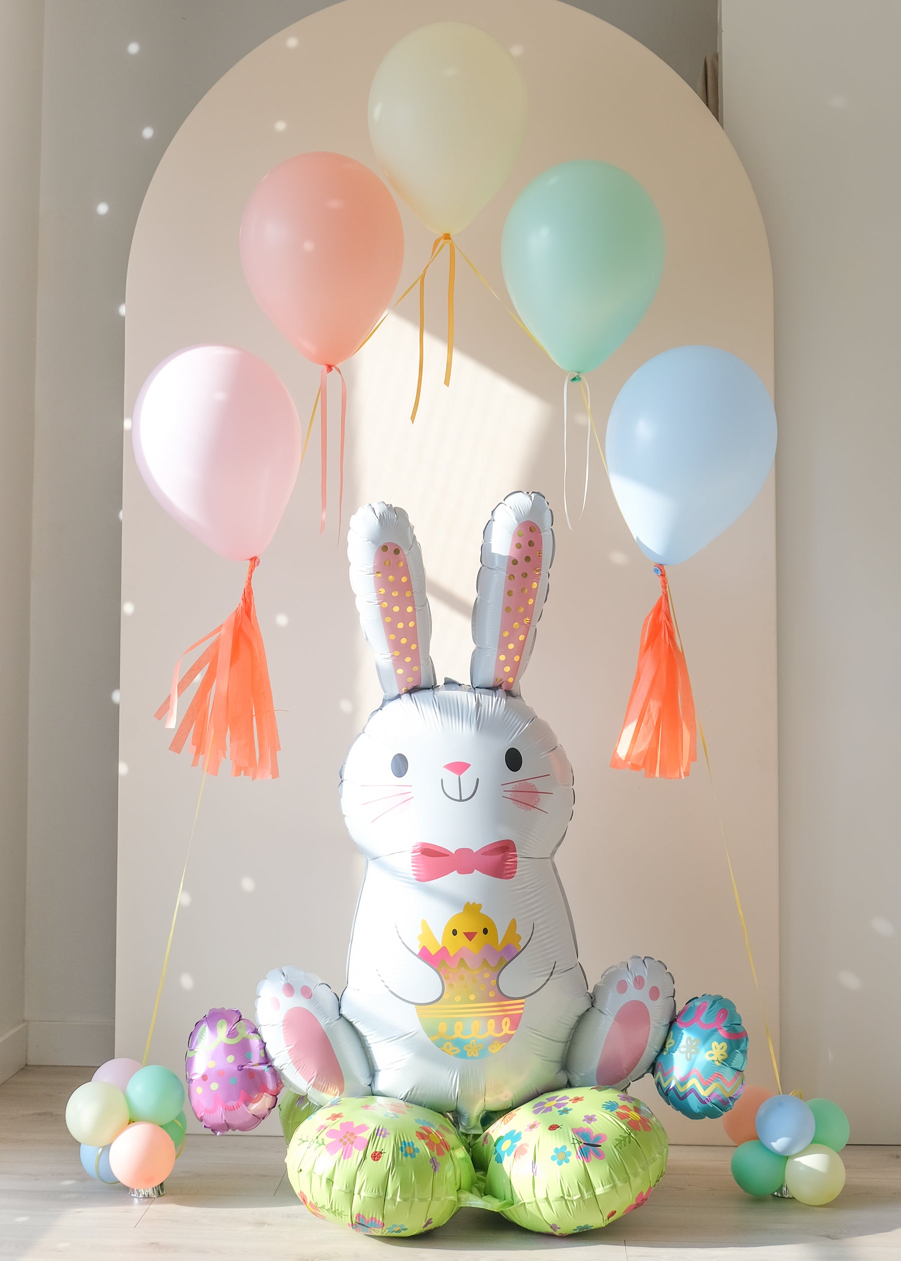 Sitting easter bunny balloon with an arch of floating pastel balloons