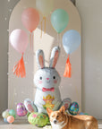 Sitting easter bunny balloon with an arch of floating pastel balloons, with a corgi dog in front for scale