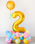 A balloon cloud with a large gold number 2 in the center, surrounded by multicolored balls in shades of pink, yellow, and blue.