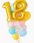 A balloon bouquet featuring a large gold number 18 balloon, with smaller multicolored balloons including pink, blue, and yellow, all adorned with confetti patterns. The balloons are attached to a ribbon bow and tassel.