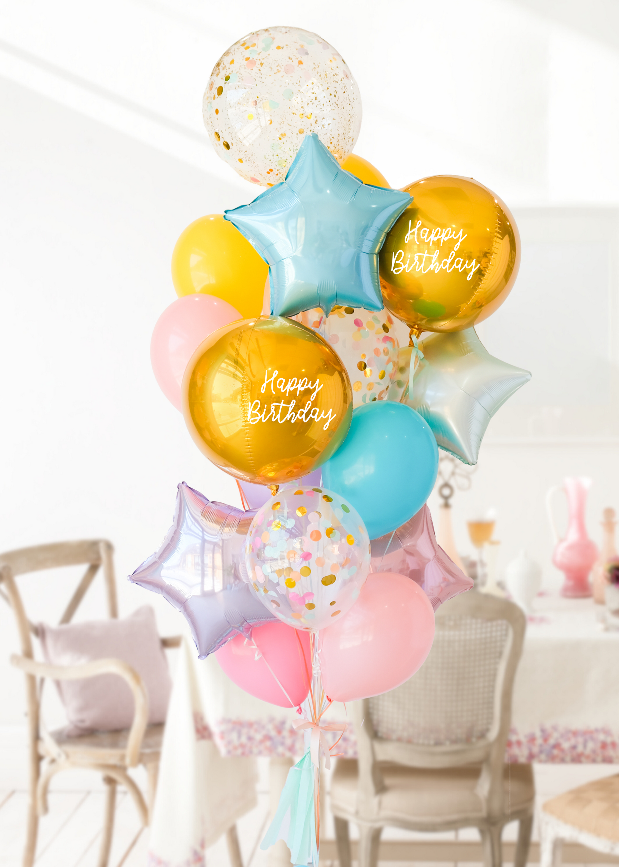 A balloon bouquet featuring two round gold orb balloon, with smaller multicolored balloons including pink, blue, and yellow, all adorned with confetti clear balloons and stars. The balloons are attached to a ribbon bow and tassel.