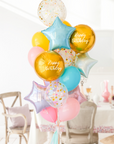 A balloon bouquet featuring two round gold orb balloon, with smaller multicolored balloons including pink, blue, and yellow, all adorned with confetti clear balloons and stars. The balloons are attached to a ribbon bow and tassel.