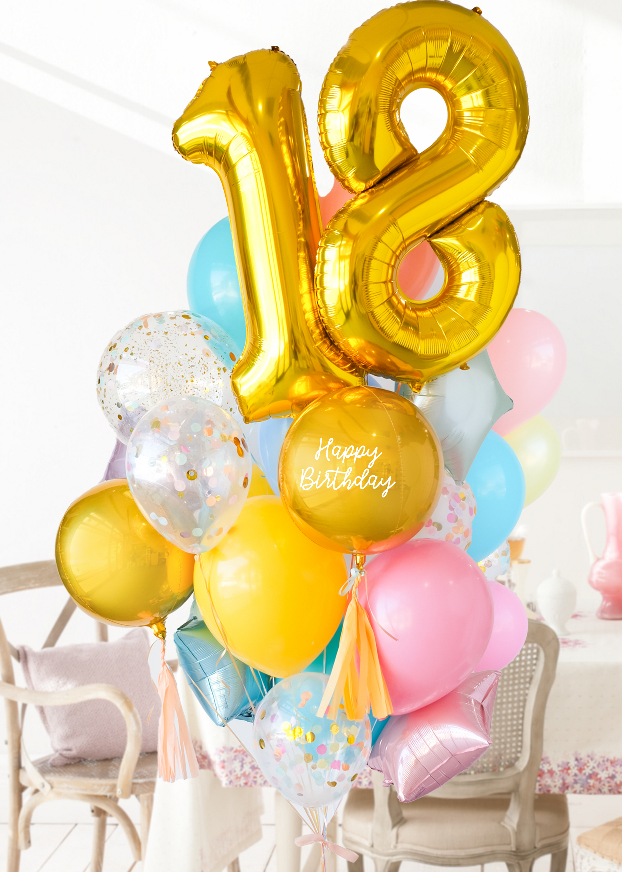 A balloon arrangement featuring a golden number '18' balloon with multicolored balloons tied to it, with the word 'Happy Birthday' printed on a gold balloon. Bouquet is in front of a dining table