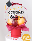 A decorative bubble balloon box with 'Class of 2025' printed on it, filled with multicolored balloons, mounted on a black stand.
