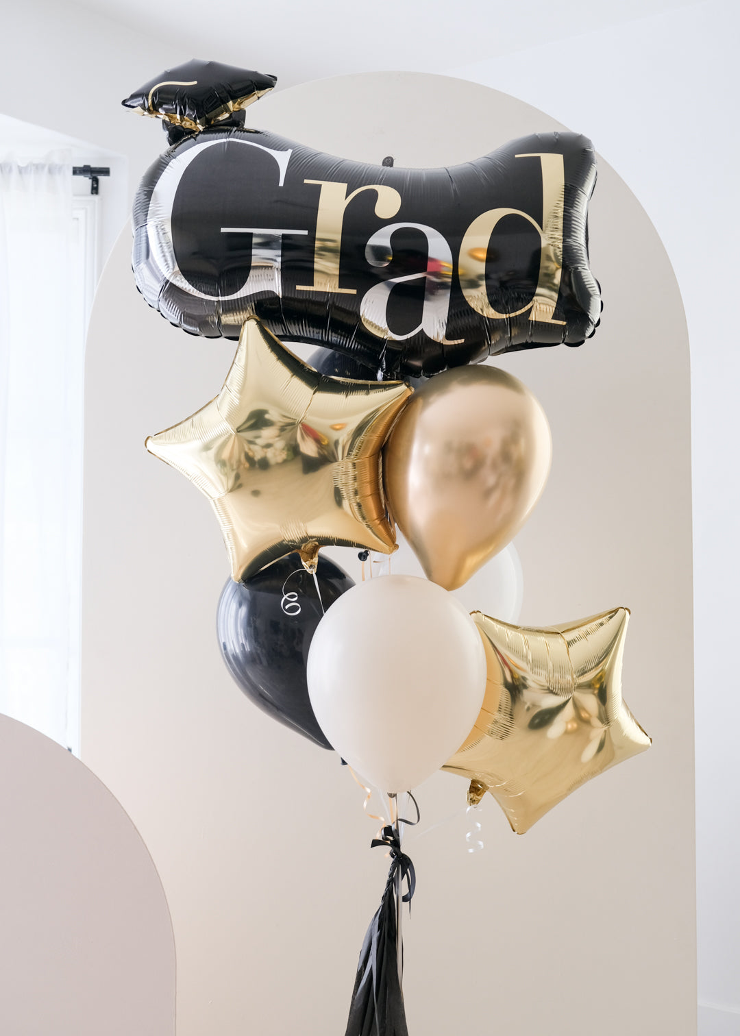 A balloon bouquet with black, gold, and silver balloons, including one that reads 'Grad' and star-shaped ones.