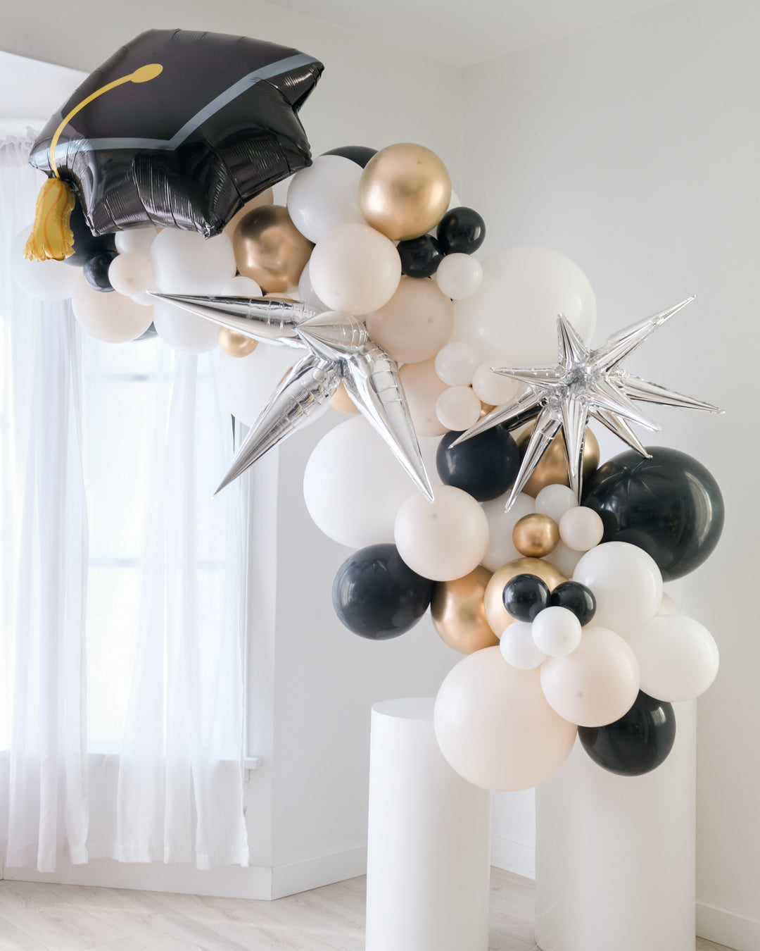 Another view of balloon garland featuring a graduation cap design, with a mix of gold, silver, and white balloons, displayed indoors.