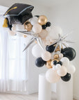 Another view of balloon garland featuring a graduation cap design, with a mix of gold, silver, and white balloons, displayed indoors.
