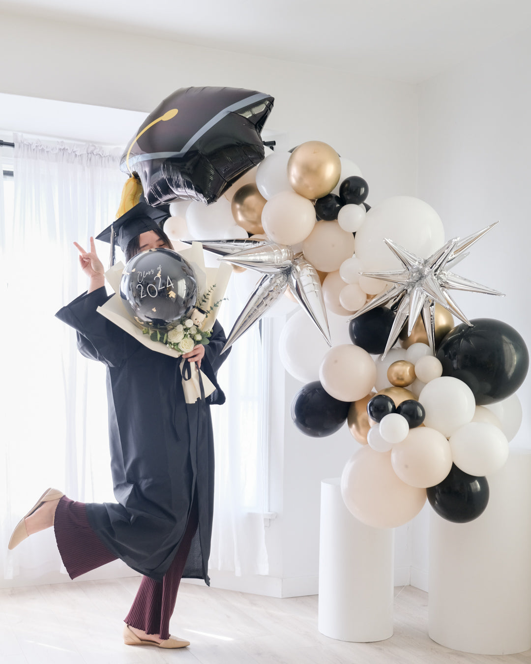 A balloon garland featuring a graduation cap design, with a mix of gold, silver, and white balloons, displayed indoors.