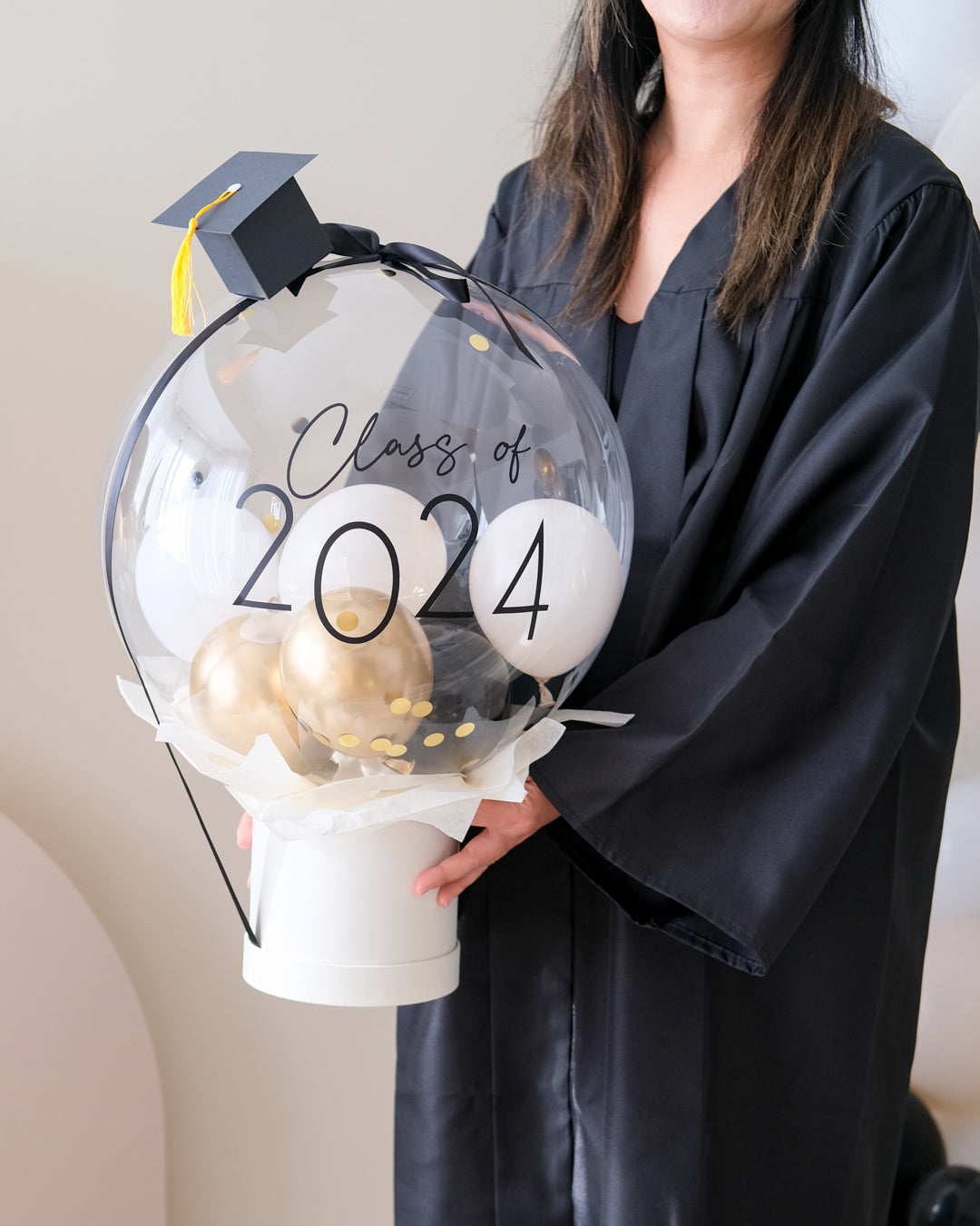 A decorative bubble balloon box with 'Class of 2025' printed on it, filled with multicolored balloons, mounted on a black stand.
