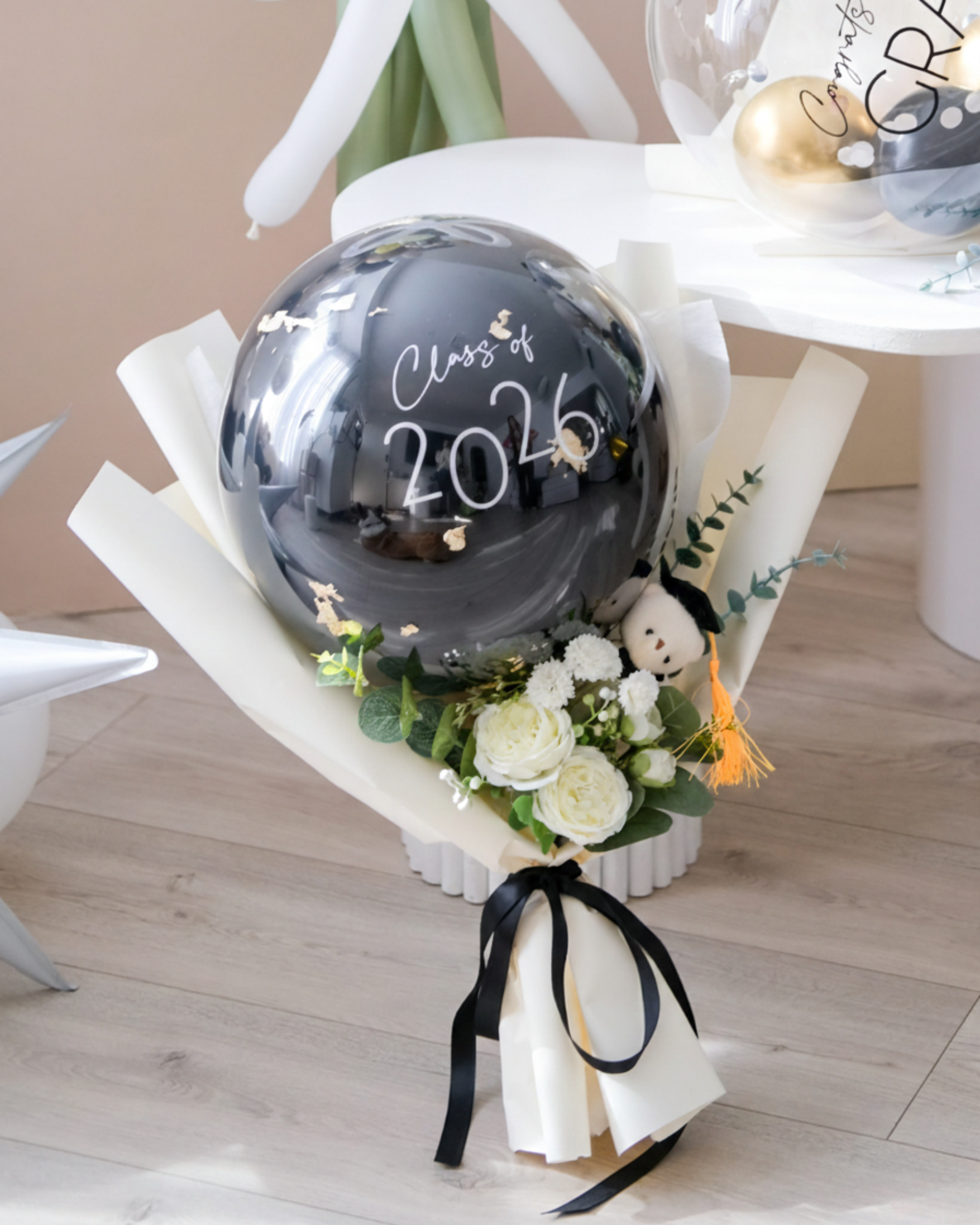 Bouquet with a black balloon featuring 'Class of 2026' text on a wooden floor.