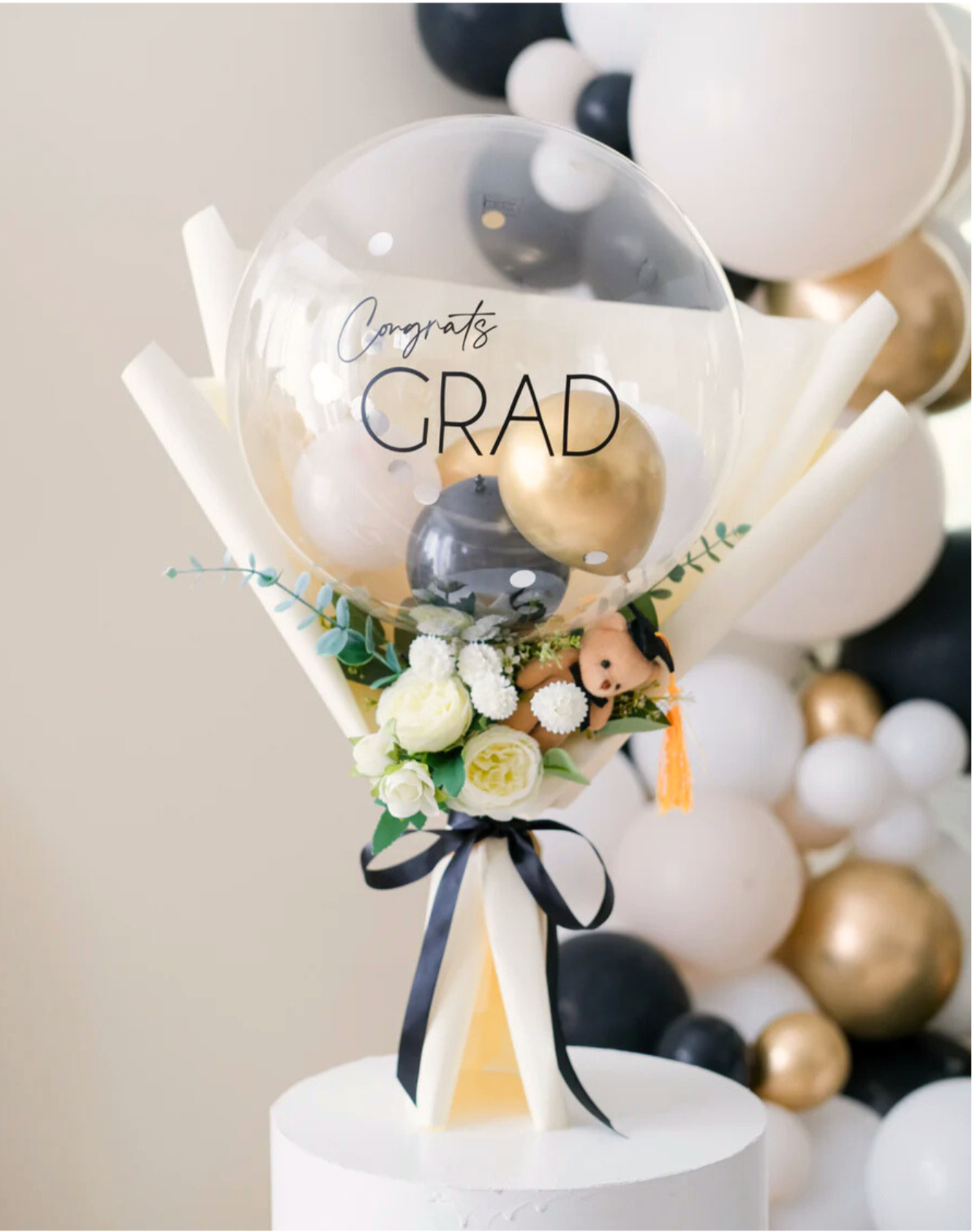 Graduation-themed balloon bouquet with 'Congrats GRAD' balloon and flowers on a stand.