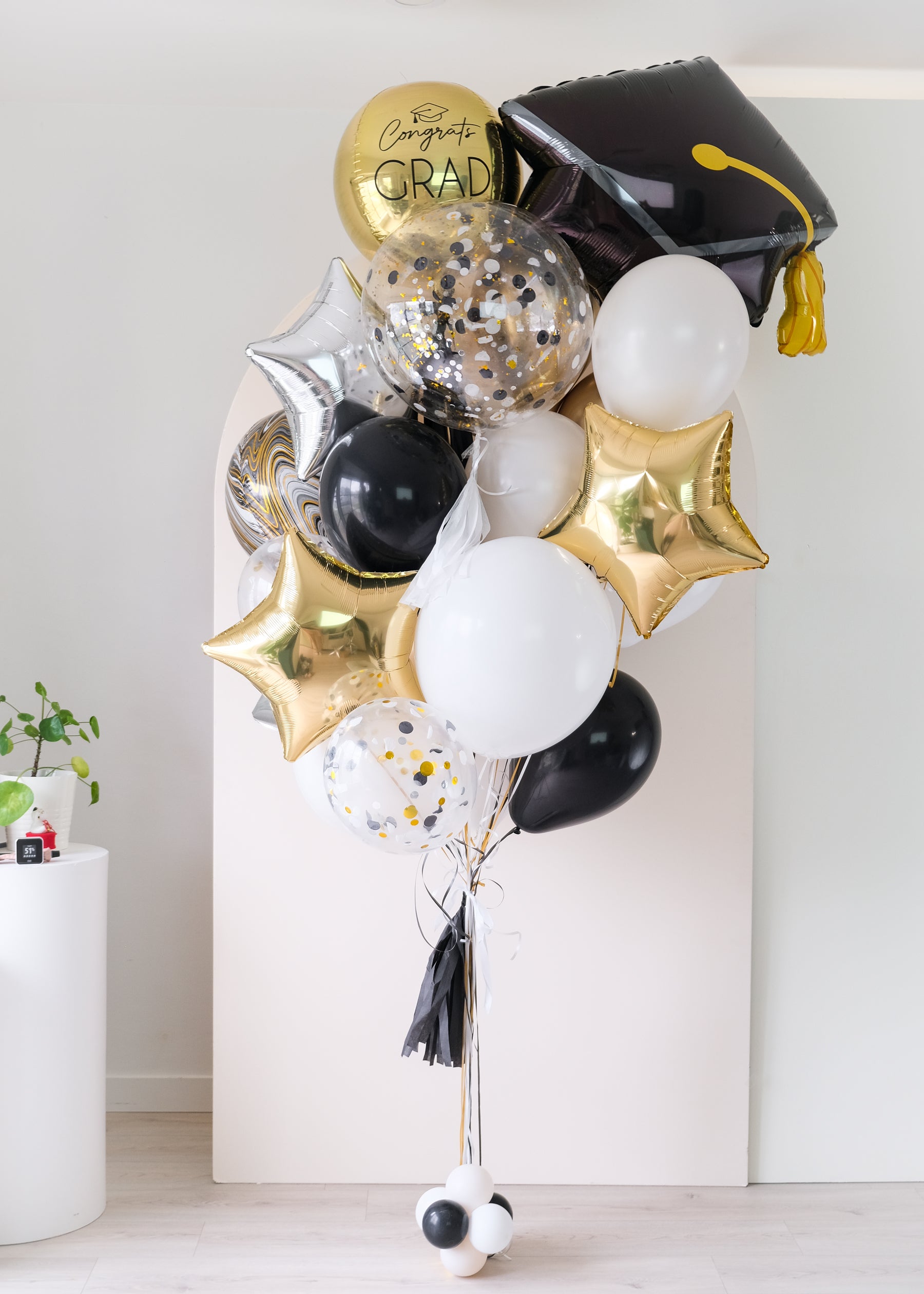 Graduation-themed balloons with a black cap, gold confetti, and foil stars with a tassel on a light background 