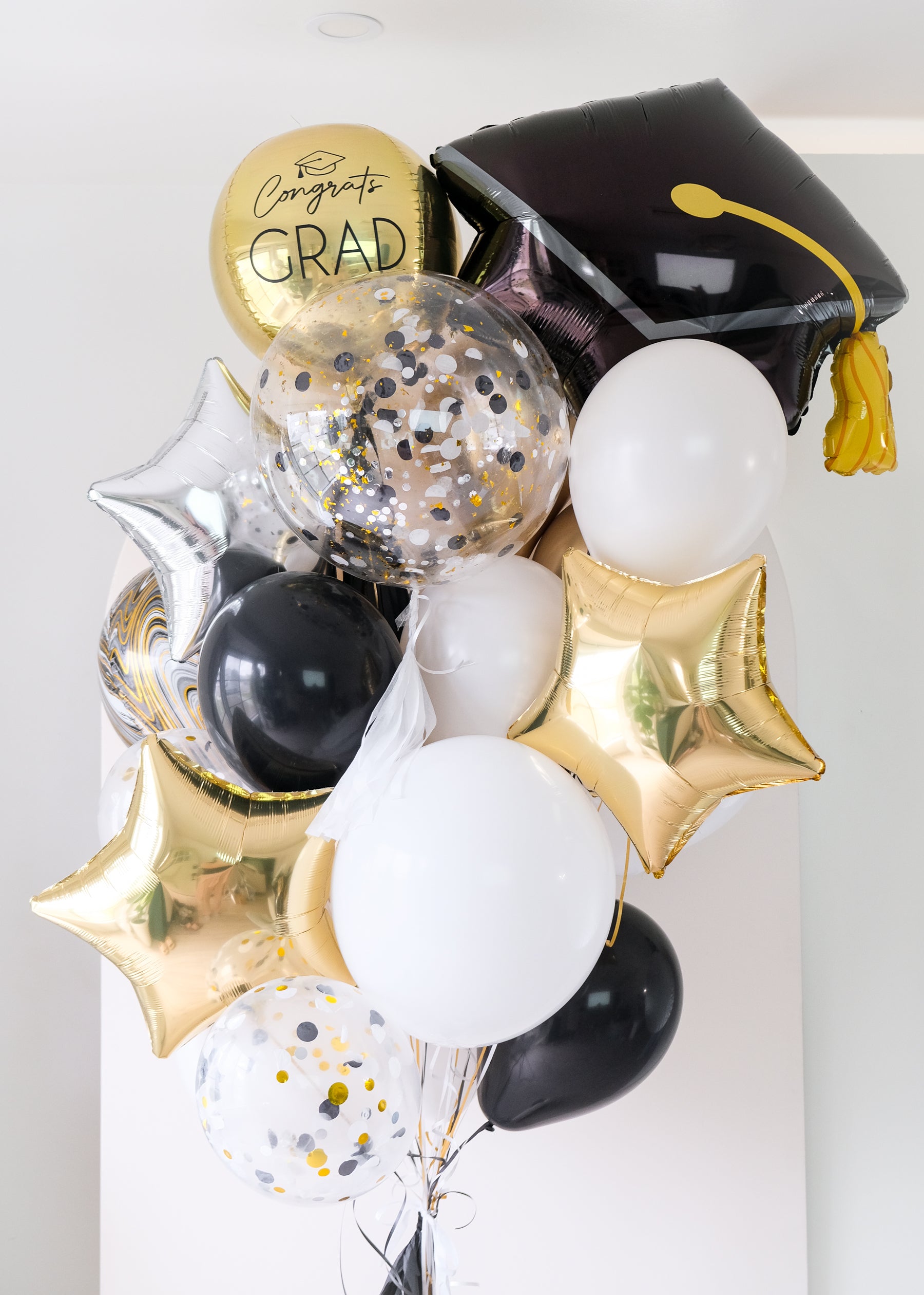 Graduation-themed balloons with a black cap, gold confetti, and foil stars on a light background