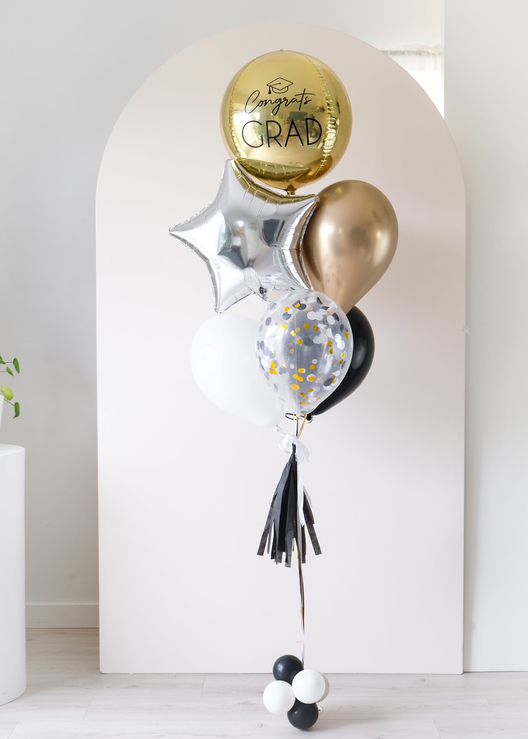 graduation balloons featuring a round gold orb, star, and latex balloons in black, gold, and white colors in front of an arch backdrop