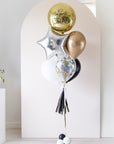 graduation balloons featuring a round gold orb, star, and latex balloons in black, gold, and white colors in front of an arch backdrop