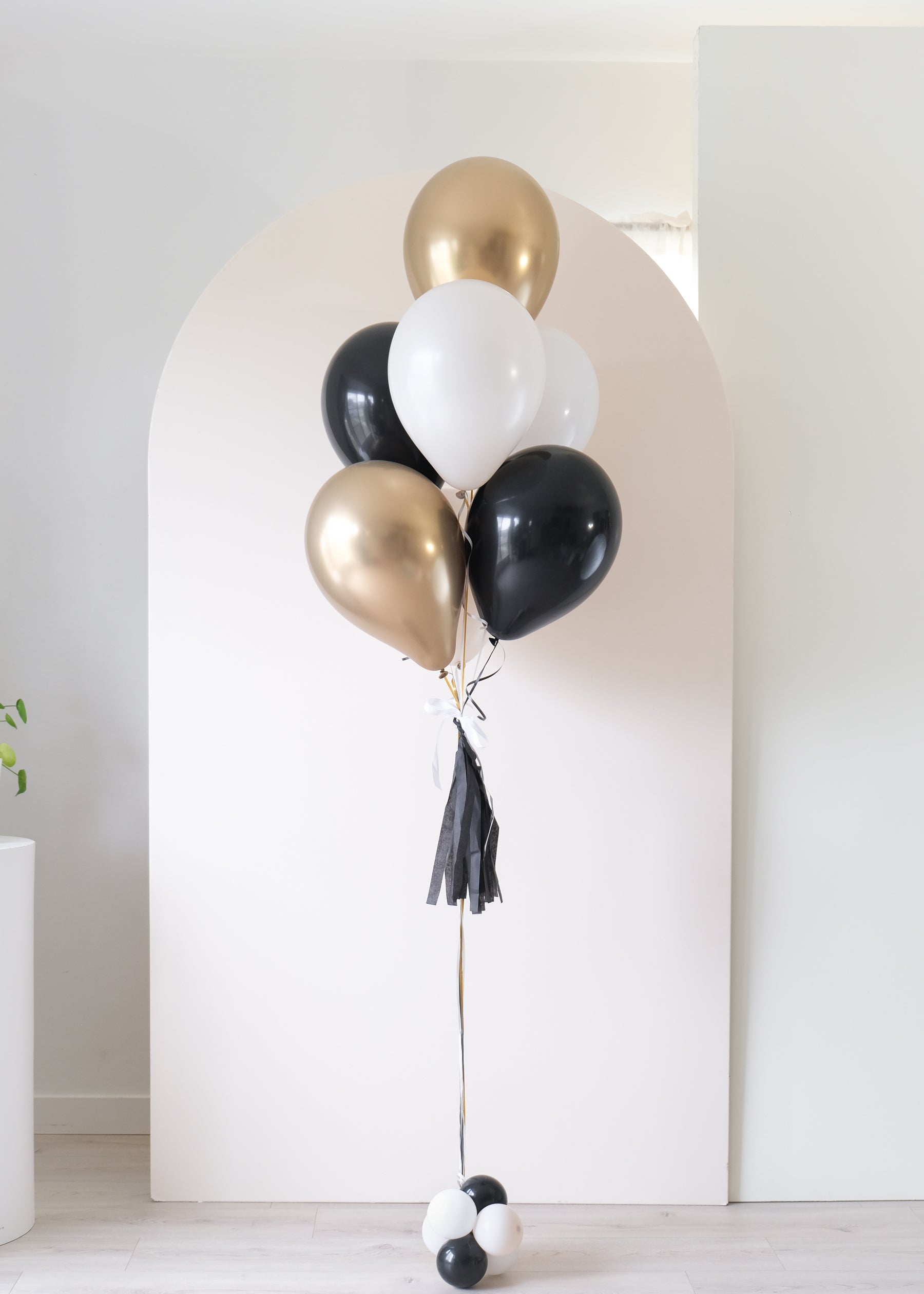 graduation balloon bouquet in black, white, cream and gold colors in front of an arch backdrop