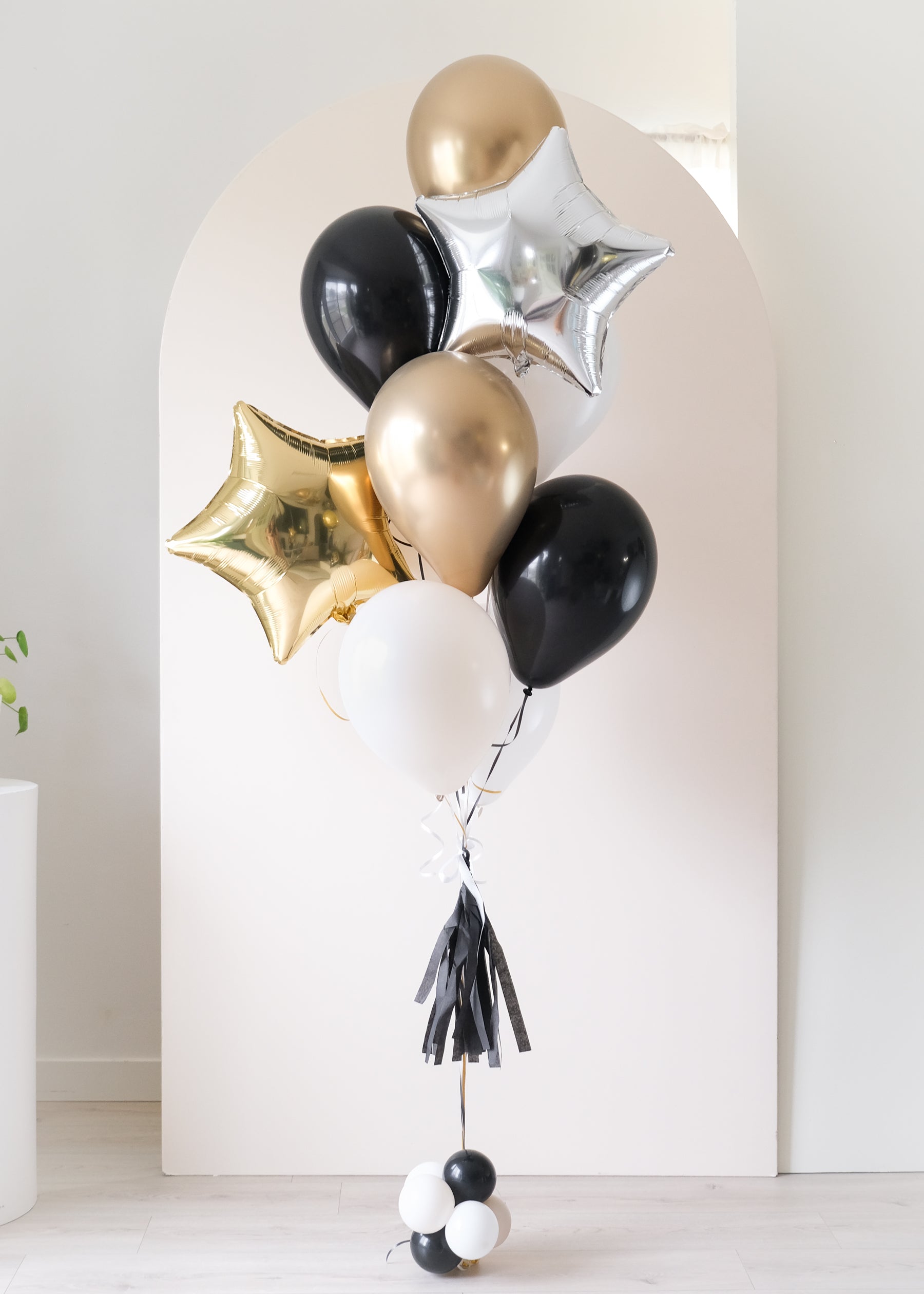 Balloon bouquet with gold, black, and silver star balloons with an arch backdrop