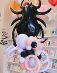 Balloon sculpture of a spider and other characters against a decorated wall.