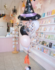 Decorative witch hat balloon with black, white, and pink balloons in a store setting.