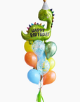 A balloon bouquet featuring a green dinosaur-shaped balloon with a 'Happy Birthday' message, surrounded balloons in various colors, tied together with a bow and tassel.