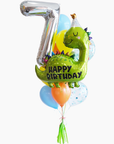 A balloon bouquet featuring a green dinosaur-shaped balloon with a 'Happy Birthday' message, surrounded balloons in various colors, tied together with a bow and tassel.