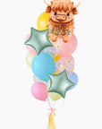A balloon bouquet featuring a Highland cow balloon with the text 'heard it was your birthday' and over a dozzen coordinating balloons including a yellow round balloon, pastel blue and pink balloons, and two light blue star-shaped balloons with confetti.