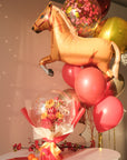 Lunar new year themed florals inside a balloon with tangerines and red envelopes on a table, with a horse balloon bouquet in the background