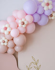 A balloon garland featuring a progression of colors from purple to pink, with decorative flower accents.