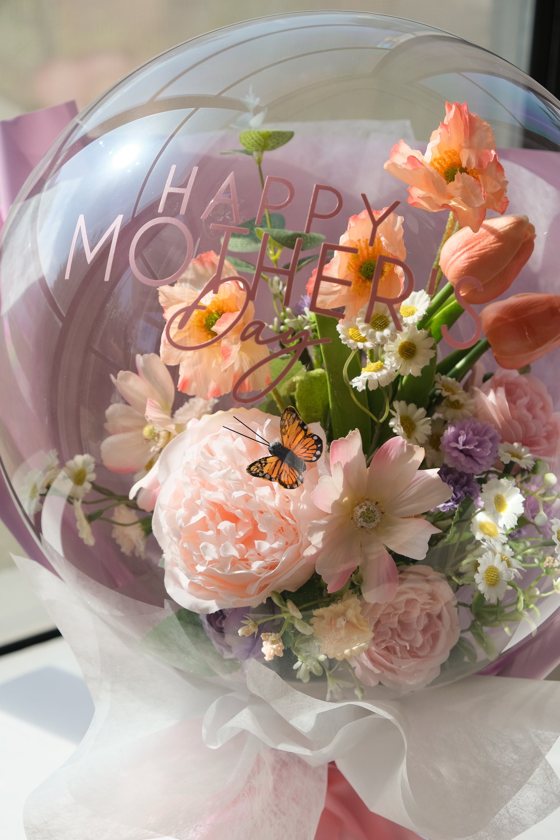 Close up of bouquet of faux spring flowers in a transparent balloon featuring a small butterfly 
