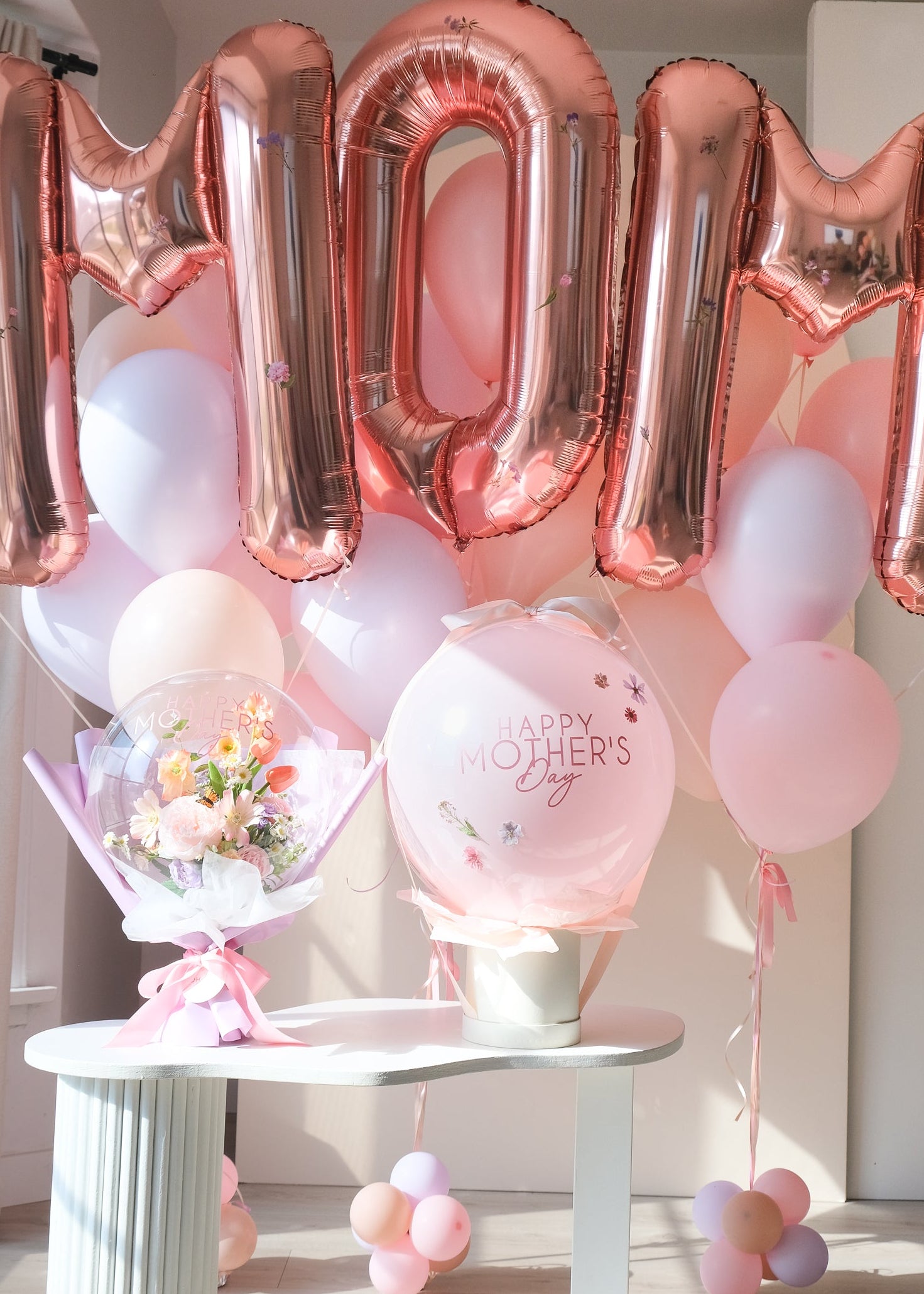 MOM rose gold balloons with a flower balloon bouquet and a round pink "Happy Mother's Day " balloon on a table
