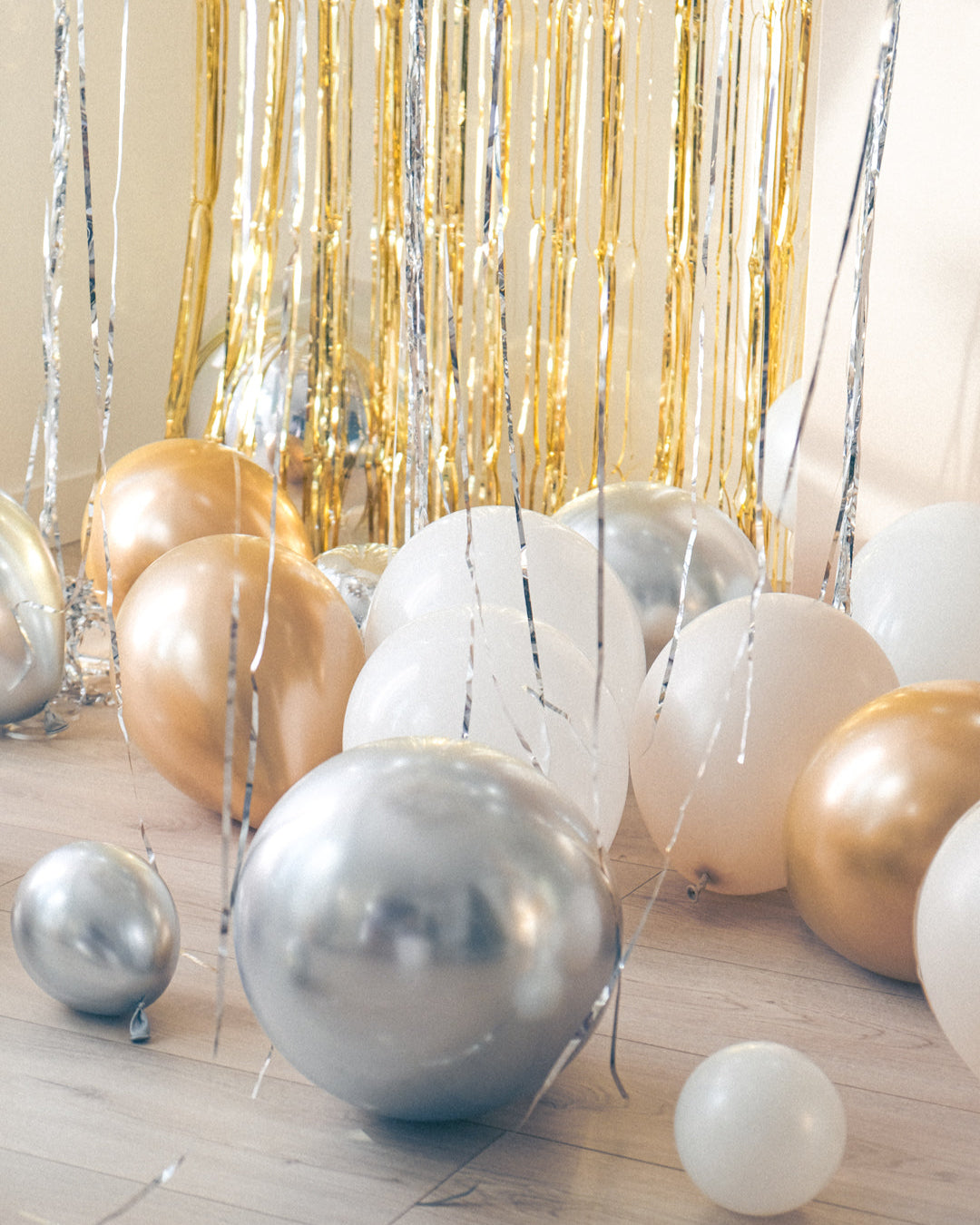 Cream, white, gold and silver balloons on the floor with a gold tinsel curtain and cream backdrop
