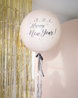 Cream round balloon with black bow and silver metallic tinsel. Text reads "3..2..1.. Happy new Year!" with gold tinsel and cream backdrop