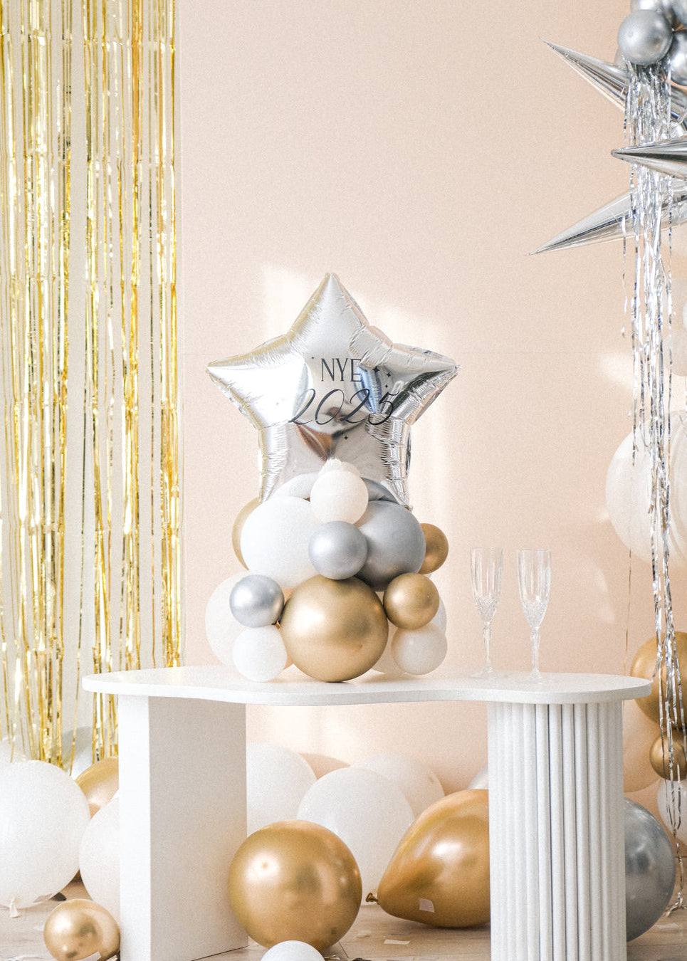 A balloon centerpiece featuring a shiny star-shaped balloon, placed on a white table with gold-colored balloons and star-shaped decorations in the background.