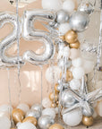 A balloon galrand in shiny silver, gold, white and creams with metallic tinsel and spikey balloon accents against a cream backdrop and silver numbers 25 to the left