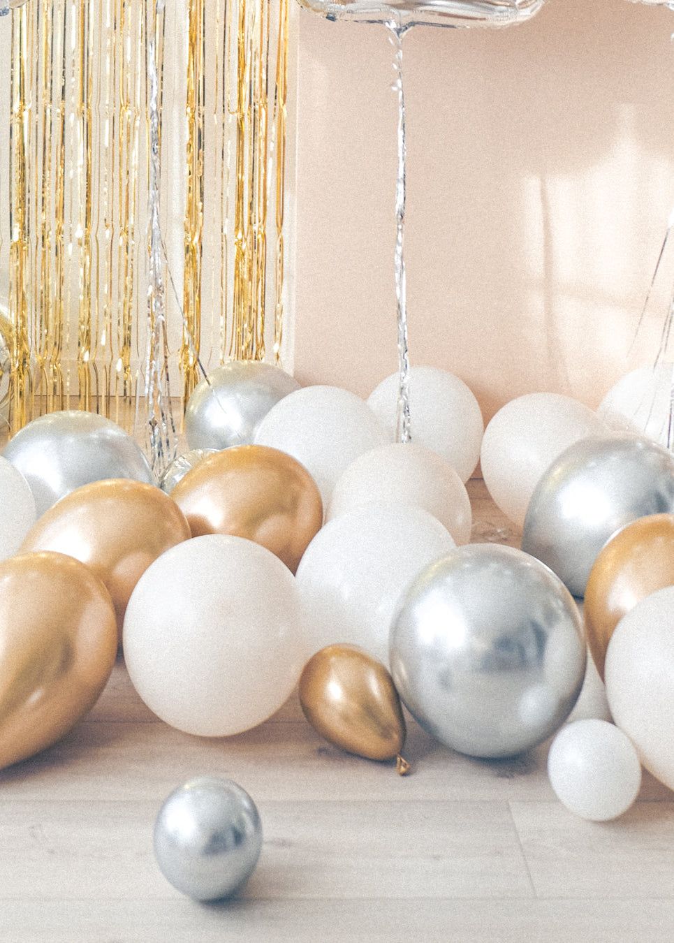 Cream, white, gold and silver balloons on the floor with a gold tinsel curtain and cream backdrop