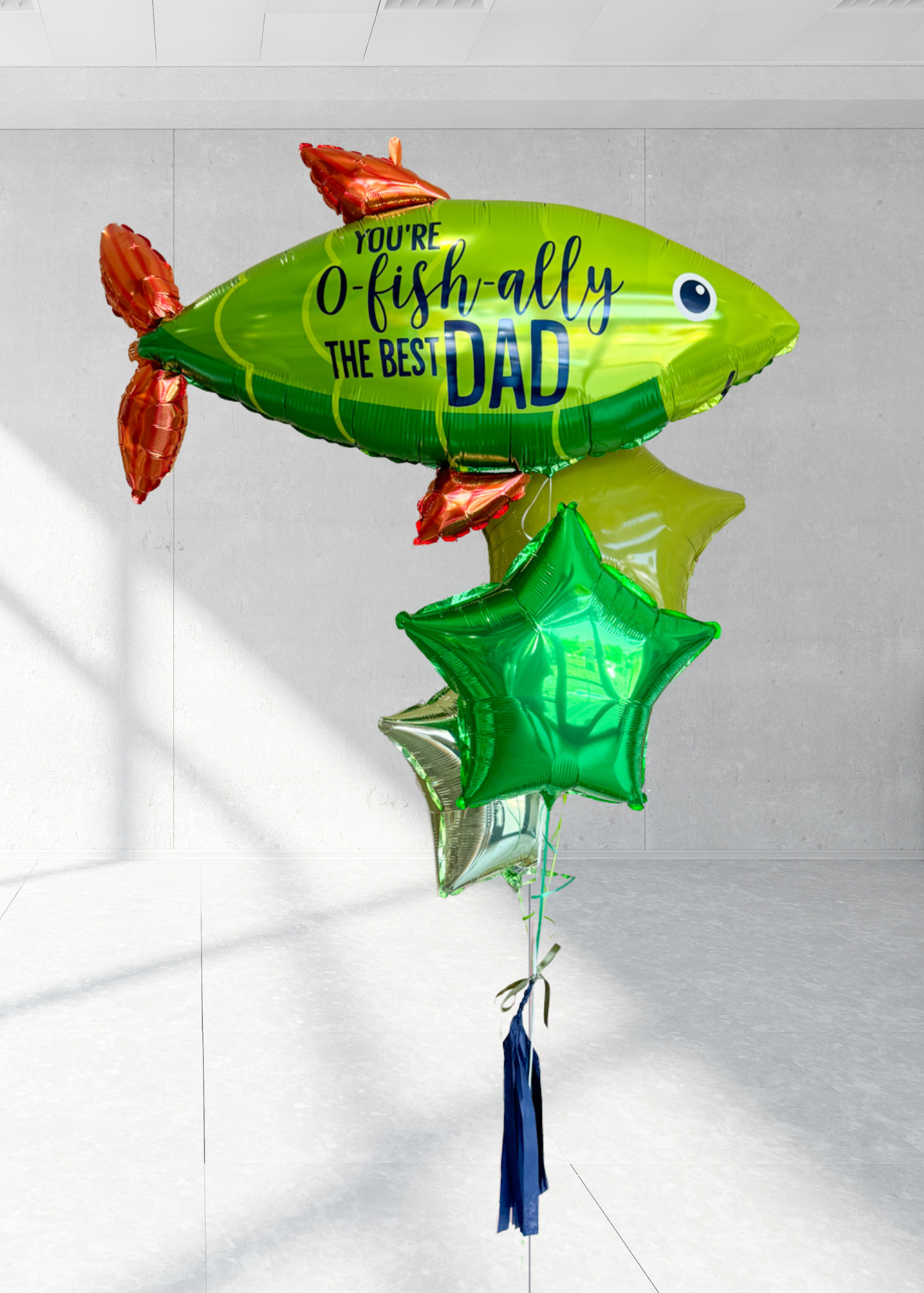 A bunch of colorful balloons including a large green one with 'You-O-Fish-ally The Best Dad' printed on it, along with various other balloons in shades of blue and red.