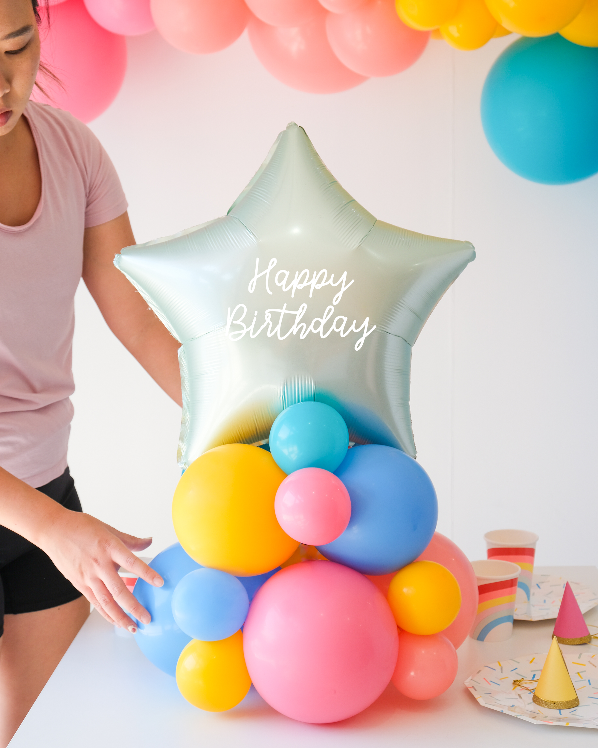 Mint colored star balloon on a cluster of rainbow latex balloons sitting on the table as a centerpiece. Text reads "Happy Birthday"