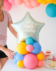 Mint colored star balloon on a cluster of rainbow latex balloons sitting on the table as a centerpiece. Text reads "Happy Birthday"