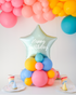 Mint Star balloon on a cluster of rainbow latex balloons sitting on the table as a centerpiece. Text reads "Happy Birthday"