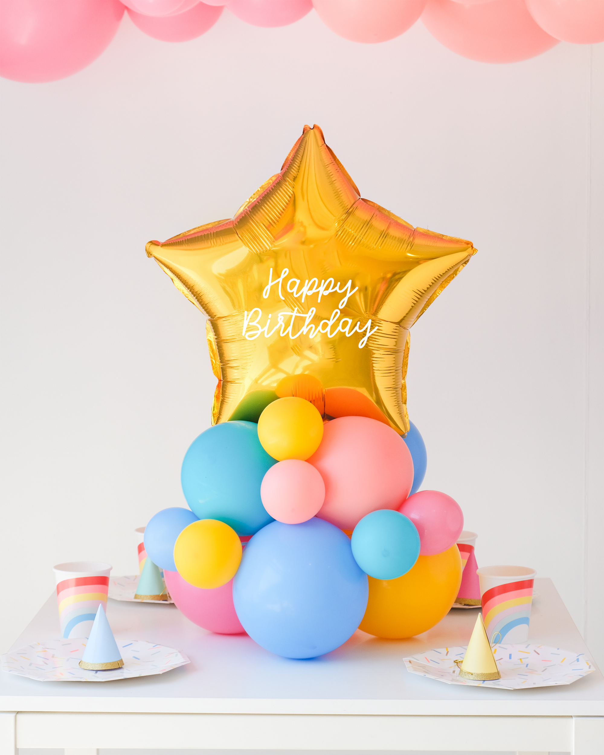 Star balloon on a cluster of rainbow latex balloons sitting on the table as a centerpiece. Text reads "Happy Birthday"