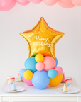 Star balloon on a cluster of rainbow latex balloons sitting on the table as a centerpiece. Text reads "Happy Birthday"