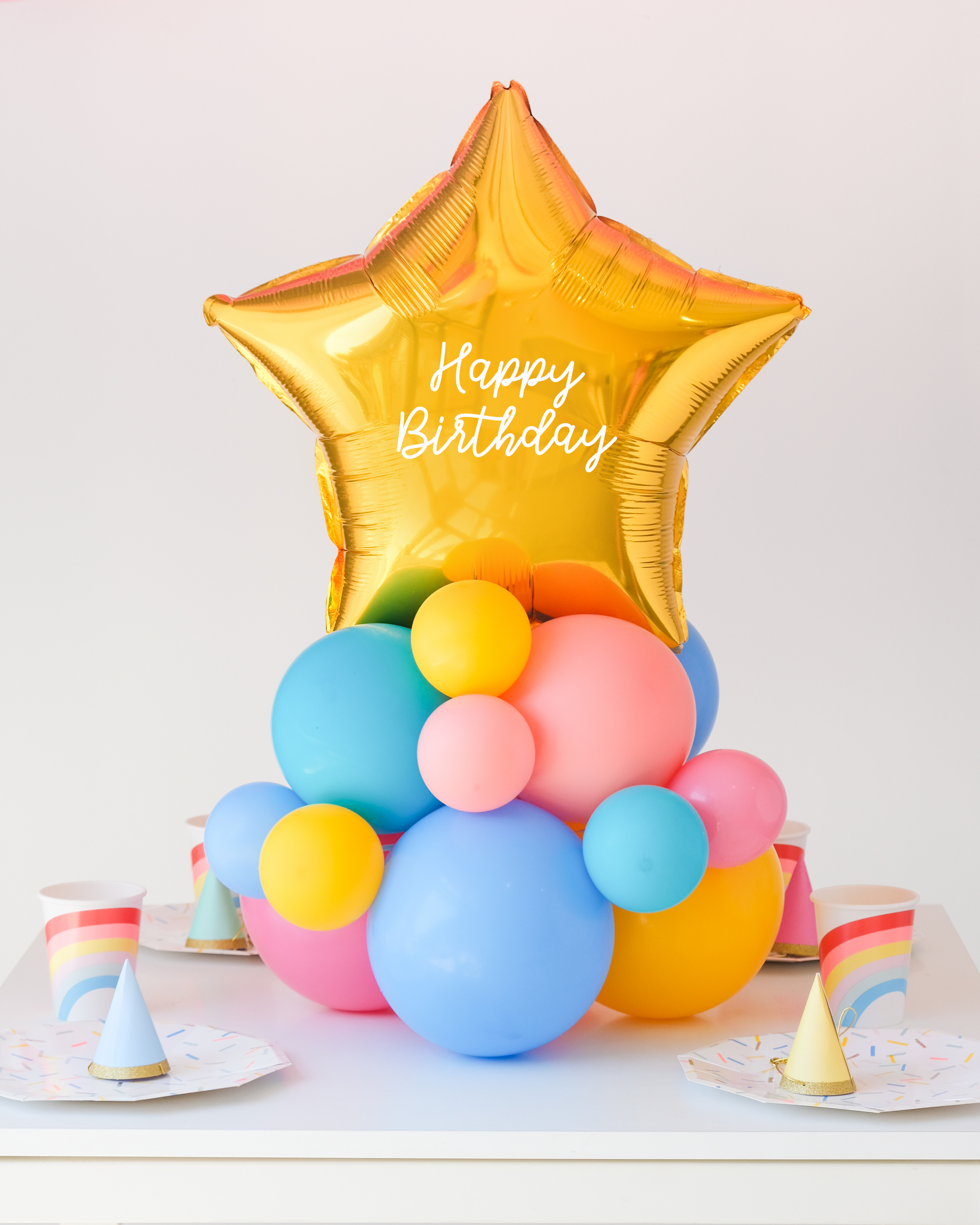 Star balloon on a cluster of rainbow latex balloons sitting on the table as a centerpiece. Text reads "Happy Birthday"