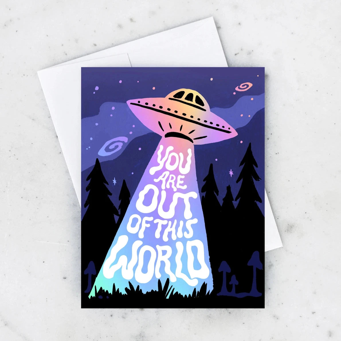 Greeting card with a spaceship shining a light into the forest. Text in squiggly style font reads "you are out of this world"