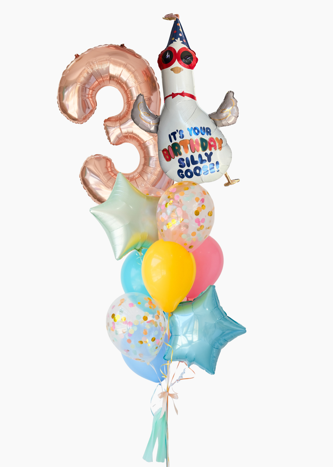 A cluster of foil balloons for a 3rd birthday celebration, featuring a metallic rose gold number 3 balloon, a white cartoon goose wearing a party hat with red sunglasses and the text 'IT'S YOUR BIRTHDAY SILLY GOOSE!', pastel balloons in yellow, pink, and light blue, and two light blue star-shaped balloons, all tied together with a white ribbon and tassel against a plain white background.