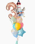 A cluster of foil balloons for a 3rd birthday celebration, featuring a metallic rose gold number 3 balloon, a white cartoon goose wearing a party hat with red sunglasses and the text 'IT'S YOUR BIRTHDAY SILLY GOOSE!', pastel balloons in yellow, pink, and light blue, and two light blue star-shaped balloons, all tied together with a white ribbon and tassel against a plain white background.