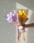 lavender and goldenrod balloon daises being held by hand in front of a white wall 