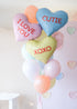 A bunch of heart-shaped balloons in various colors with love-related phrases written on them, such as 'I LOVE YOU' and 'XOXO'.