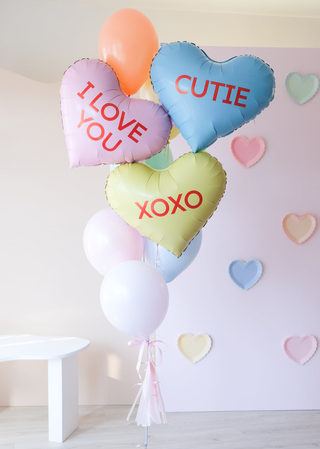 A bunch of heart-shaped balloons in various colors with love-related phrases written on them, such as 'I LOVE YOU' and 'XOXO'.