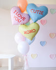 A bunch of heart-shaped balloons in various colors with love-related phrases written on them, such as 'I LOVE YOU' and 'XOXO'.