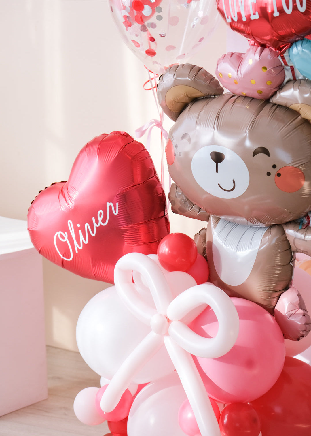 Close up image of a Valentine's Day balloon present featuring a heart-shaped balloon with the name 'Olivia', a teddy bear holding balloons
